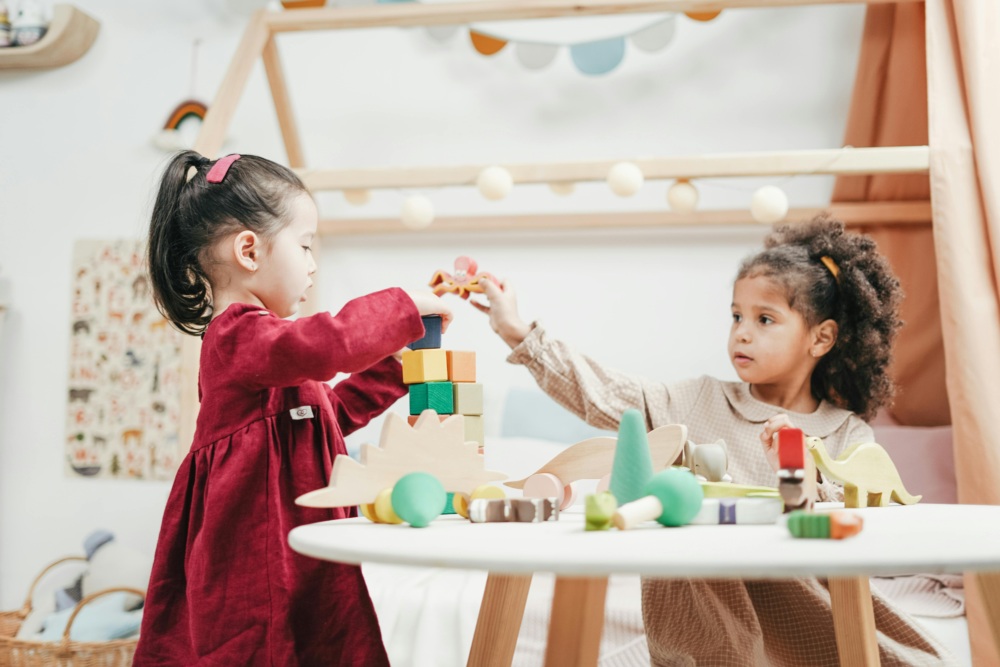 Two little girls playing with wooden blocks in a room.